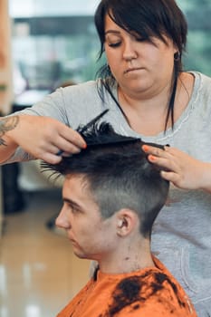 Hairdresser haircutting styling young man's hair in barbershop. Young woman working as a hairdresser in hair salon. Real people, authentic situations