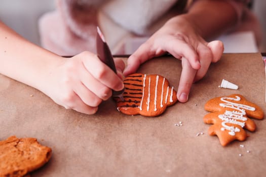 Girl decorating baked Christmas gingerbread cookies with chocolate writing pen