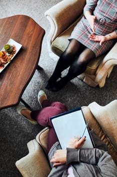 Professional psychologist doctor giving the consult to female patient. Close shot from above of two women during psychotherapy session. Therapist writing down notes during meeting with her female patient. Consulting and therapy concept. Real people, authentic situations