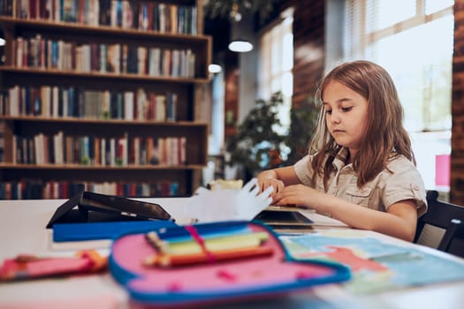 Schoolgirl learning, playing, doing puzzles and reading book in school library. Primary school pupil is engaged in book with jigsaw. Smart girl learning from book. Benefits of everyday reading. Child curiosity