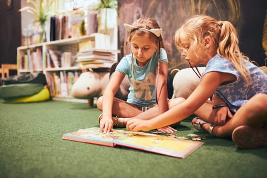 Two elementary schoolgirls solving puzzles and riddles in school library. Students learning from books. Pupils having fun in library. Back to school