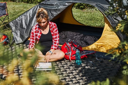 Woman planning next trip while sitting with map in tent. Woman relaxing in tent at camping during summer vacation. Actively spending vacations outdoors close to nature. Concept of camp life