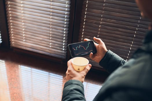 Person investing trading on stock cryptocurrency market using investing application on smartphone. Stock market investment in hand. Trader holding mobile phone looking at candle chart