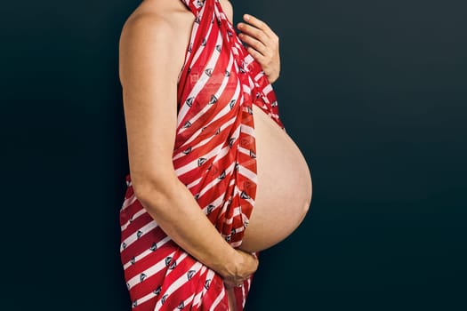 Pregnant woman touching her tummy standing over plain background. Pregnancy, expectation, motherhood concept