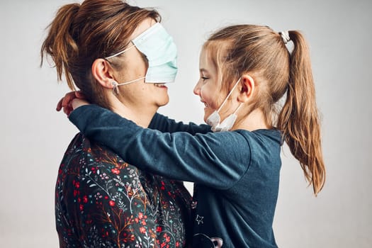 Little girl kissing her mother who has covered eyes with face mask for fun. Daughter giving kiss her mom during covid-19