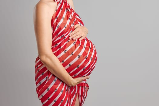 Pregnant woman touching her tummy standing over plain background. Pregnancy, expectation, motherhood concept