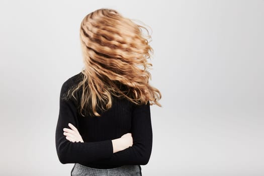 Portrait of pretty cheerful young woman waving tossing her hair holding arms crossed standing over a grey plain background