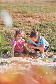 Children, little girls and boy, playing in sandbox in playground outside on summer day. Real people, authentic situations