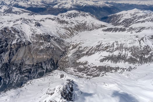 aerial landscape, from a glider plane, of hairpin turns at Stelvio pass road  among rocky snowy slopes, shot from south west in bright late spring light, Sondrio, Italy