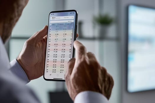 A professional reviews his schedule on a smartphone calendar in a sleek office during work hours, planning the day ahead.