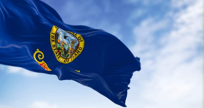 Idaho state flag fluttering in the wind. Blue background with the state seal and a red band with State of Idaho in gold text. 3d illustration render. Selective focus. Close-up