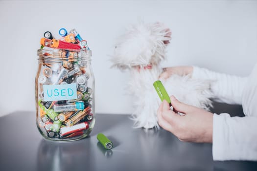 Little girl removing used batteries from toy and putting into jar for recycling. Child separating waste. Batteries only container. Jar filled with discharged used batteries. Waste disposal and recycling. Separating the waste. Batteries only container