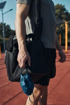 Young man standing in street workout calisthenics park holding the face mask need to avoid virus infection and to prevent the spread of disease in time of coronavirus