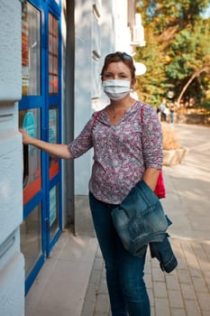 Woman standing at front of pharmacy, wearing face mask to cover mouth and nose during pandemic coronavirus outbreak, looking at camera