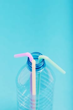 Plastic bottle with colorful straws over blue background. Collecting plastic waste to recycling. Concept of plastic pollution and too many plastic waste. Copy space at the top