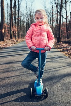 Little girl playing in the park, riding a scooter, having fun on sunny autumn day. Real people, authentic situations