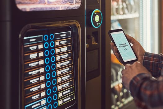 Consumer paying for product at vending machine using contactless method of payment with mobile phone. Man using payment app on smartphone to buy product. Male hand holding smart phone with payment confirmation on screen