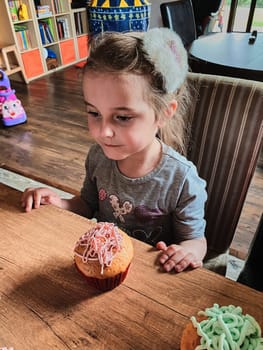 Group of children baking cupcakes, squeezing cream from confectionery bag, preparing ingredients, topping, sprinkles for decorating cookies. Kids cooking, working together in kitchen at home. Concept of happy family