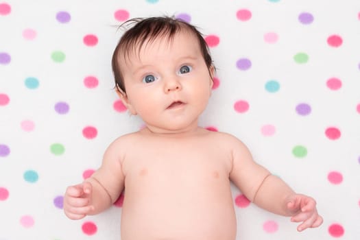 Little baby girl lying on blanket with colourful polka dots