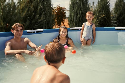 Children splashing, jumping, playing in a pool in backyard on summer vacation day. Real people, authentic situations