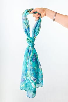 Female hand holding silk colourful hand painted tied scarf over grey background. Woman fashion, tying a scarf, wearing a scarves. Stylish ways to tie and wear scarves