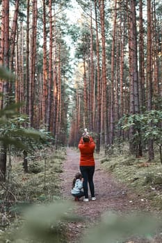 Mother and her little daughter walking in a forest during summer vacation trip. Woman taking photos using smartphone. Family spending time together outdoors in nature