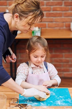 Little girl rolling the dough with her moms help for the cake. Kid taking part in baking workshop. Baking classes for children, aspiring little chefs. Learning to cook. Combining and stirring prepared ingredients. Real people, authentic situations
