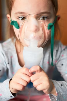 Sick little girl having medical inhalation treatment with nebuliser. Child with breathing mask on her face sitting in bed