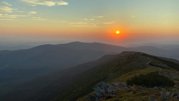 Sunrise in mountains. Natural mountain landscape with illuminated misty peaks, foggy slopes and valleys, blue sky with orange yellow sunlight. Amazing scene from Beskid Zywiecki in Poland