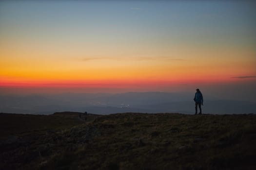 Man admiring sunrise. Mountains at sunrise. Man standing on peak. Natural mountain landscape with illuminated misty peaks, foggy slopes and valleys, blue sky with orange yellow sunlight. Amazing scene from Beskid Zywiecki in Poland