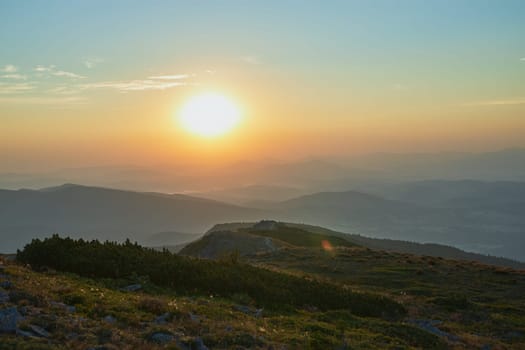Sunrise in mountains. Natural mountain landscape with illuminated misty peaks, foggy slopes and valleys, blue sky with orange yellow sunlight. Amazing scene from Beskid Zywiecki in Poland