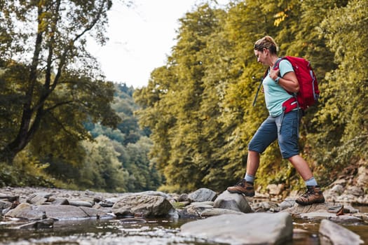 Traveling trekking with backpack concept image. Backpacker female in trekking boots crossing mountain river. Woman hiking in mountains during summer trip. Vacation trip close to nature. Natural scenery