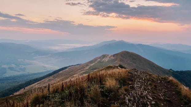 Sunset in mountains. Natural mountain landscape with illuminated misty peaks, foggy slopes and valleys, blue sky with orange yellow sunlight. Amazing scene from Bieszczady Mountains in Poland