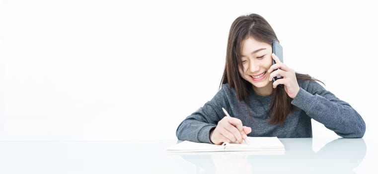 Close up woman long hair writing notebook and using mobile phone on white background