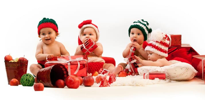 Four cute babies in xmas costumes playing among gifts