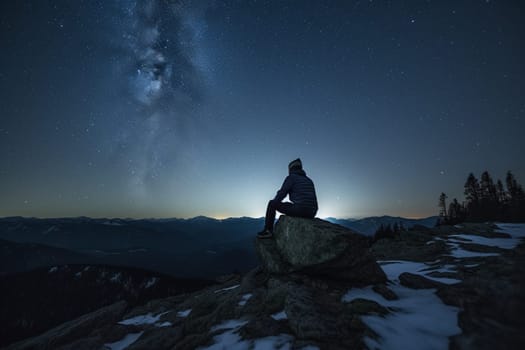 A man lies on his back on a mountaintop, gazing up at the vast and infinite night sky. The scene is mystical and powerful, with the grandeur of the mountains and the darkness of the night adding to the sense of awe-inspiring beauty. The man is in a state of contemplation, reflecting upon his place in the universe and the vastness of existence. This scene can evoke feelings of wonder, awe, and introspection. (generative AI)