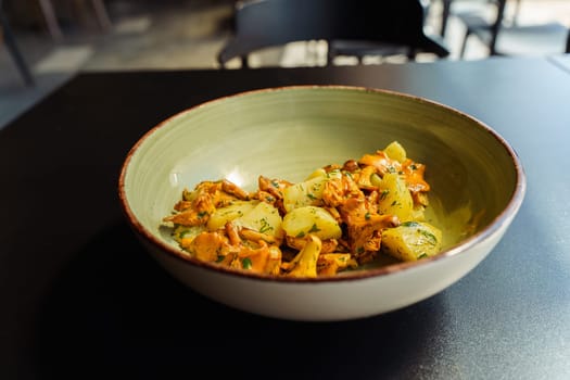 Fried chanterelles with boiled potatoes and green herbs, parsley and dill in a bowl for lunch.