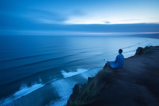 A person sits in meditation at the edge of a cliff overlooking the vast blue of the ocean. The scene is serene and calming, with the blue hour light adding to the reflective and contemplative mood. The sound of the waves crashing against the rocks and the cool breeze help create a harmonious atmosphere for inner reflection and peace. This scene can evoke feelings of calmness, serenity, and introspection. (generative AI)