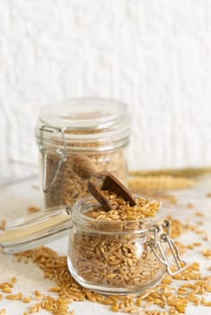 Glass jar of raw dry rye grain with a wooden spoon on white table close up. Healthy alternative low gluten seeds. Protein source for vegan and vegetarian diet.