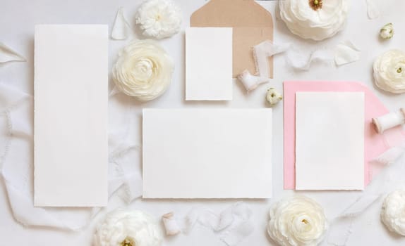 Blank cards and envelopes near cream roses and white silk ribbons top view, mockup. Romantic scene with wedding set and pastel flowers flat lay. Valentines, Spring or Mothers day concept