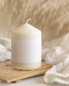 Candle with label on wooden tray near dry pampas grass and cosy white sweater Close up, copy space. Boho packaging mock up. Home decorations, Bohemian, ethnic or scandinavian style