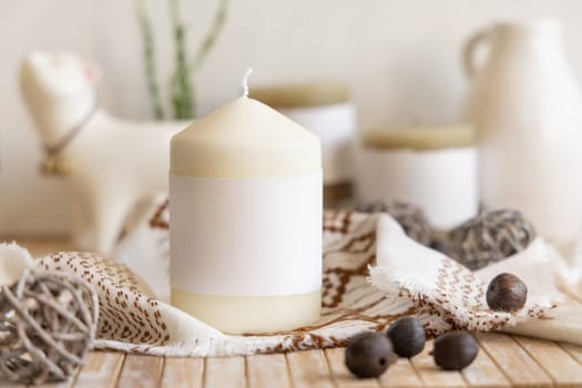 Candle with blank paper label on wooden table near natural decor Close up, copy space. Boho or ethnic packaging mock up. Home decorations in Bohemian or scandinavian style