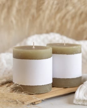 Candles with label on wooden tray near dry pampas grass and cosy white sweater Close up, copy space. Boho packaging mock up. Home decorations, Bohemian, ethnic or scandinavian style