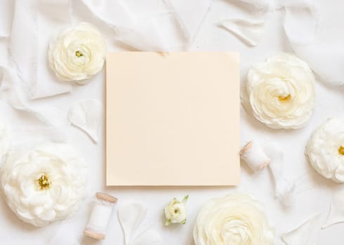 Blank card near cream roses and white silk ribbons top view, wedding mockup. Romantic scene with square card and pastel flowers flat lay. Valentines, Spring or Mothers day concept