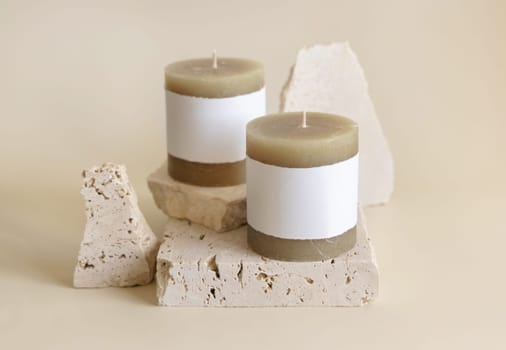 Candles with label on beige near cream travertine stones, Close up, copy space. Brand packaging mock up. Home decoration, minimal interior, Bohemian or scandinavian style