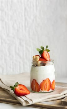 Greek yogurt, nuts and strawberries in a glass jar on a wooden tray with napkinn, close up, copy space. Healthy breakfast with fruits and nuts. Great way to eat protein