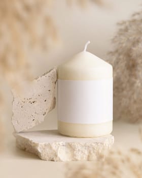 Candle with blank paper label on beige stone near dried pampas grass Close up, copy space. Boho brand packaging mock up. Home decoration, Close to nature or scandinavian style