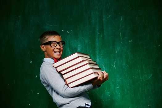 Cheerful schoolkid with stack of books looking at camera