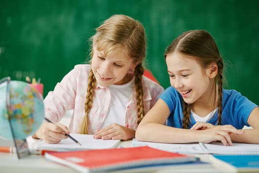 Two cute schoolgirls drawing together at lesson
