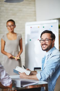 Asian businessman in eyeglasses looking at camera with smile in working environment